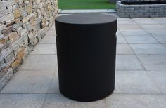 a black trash can sitting in front of a stone wall next to a grass field