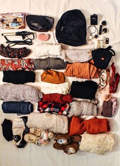 an assortment of clothing and accessories laid out on a bed top with white sheeting