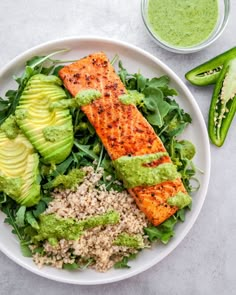 a white plate topped with salmon and rice next to a bowl of green sauce on the side