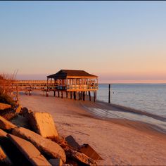 a pier on the beach at sunset with waves coming in