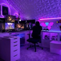 a person sitting at a desk in front of two computer monitors with neon lights on them