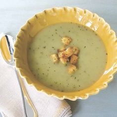 a yellow bowl filled with soup and croutons on top of a white table