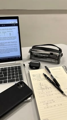 an open laptop computer sitting on top of a desk next to a notebook and pen