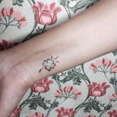 a small four leaf clover tattoo on the left wrist and right hand with pink flowers