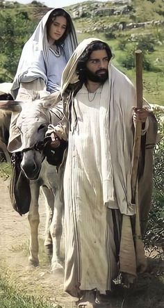 a man and woman walking down a dirt road next to a cow with a cross on it's back