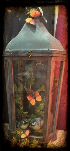 an old fashioned lantern with some flowers on it's top and two birds in the bottom