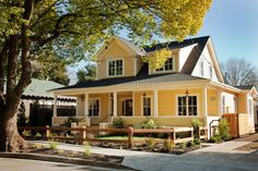 a yellow house with black roof and white trim on the front porch is surrounded by trees