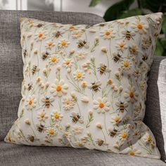 a pillow with bees and daisies on it sitting on a couch in front of a potted plant