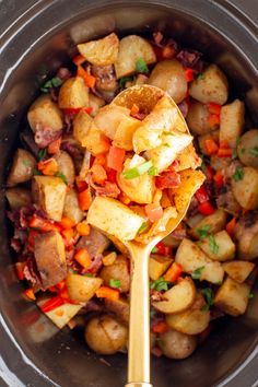 a spoon full of potatoes and carrots in a crock pot with a wooden spoon