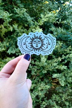 someone holding up a sticker with the sun and moon on it in front of some bushes