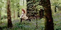 a woman is running through the woods with her hair blowing in the wind and wearing a long white coat