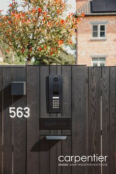 a phone is mounted to the side of a fence with numbers on it and a tree in the background