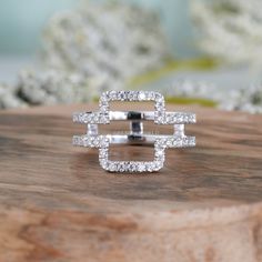 a white gold and diamond ring sitting on top of a piece of wood with flowers in the background