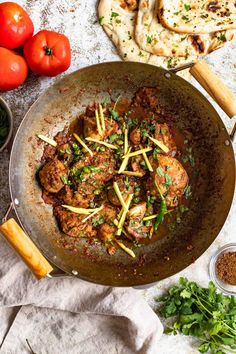 a pan filled with meat and vegetables on top of a table next to some pita bread