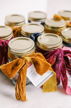 several jars with ribbons tied around them sitting on a white table top next to each other