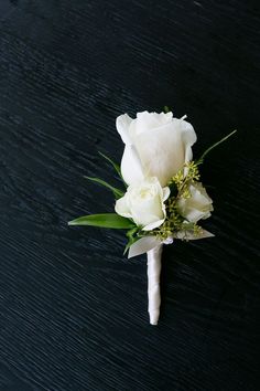 a boutonniere with white roses and greenery on a black table top