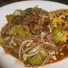 a white plate topped with meat and veggies covered in gravy next to rice