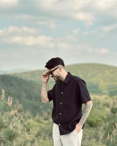 a man standing on top of a lush green hillside next to tall grass and trees