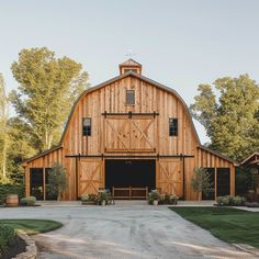 a large wooden barn sitting on top of a lush green field next to trees and bushes