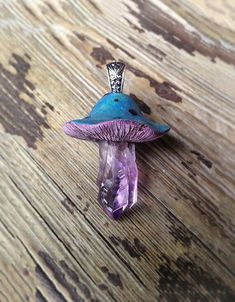 a small purple and blue mushroom sitting on top of a wooden table next to a necklace