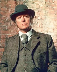 a man in a suit and hat standing next to a brick wall