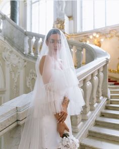 a woman in a white wedding dress and veil standing on the stairs with her bouquet