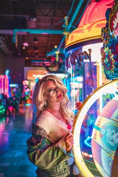 a woman standing in front of a neon sign at an amusement park with her arms crossed