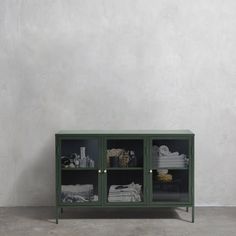 a black cabinet with glass doors in front of a white wall and grey concrete floor