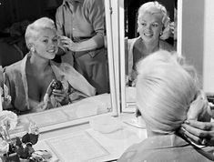 a woman is getting her hair done in front of a mirror while others look on