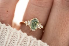 a woman's hand holding a ring with an oval shaped green and white stone