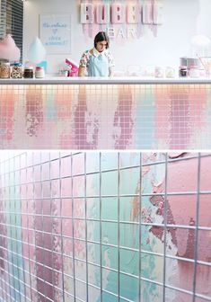 a woman standing in front of a counter with pink and blue tiles on it's walls