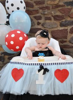 a baby sitting in a high chair next to balloons