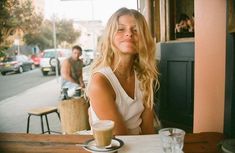 a woman sitting at a table with a cup of coffee in front of her and another man behind her