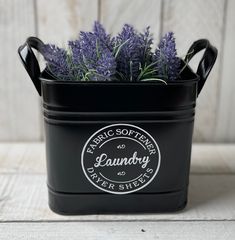 a black bucket filled with purple flowers on top of a wooden table