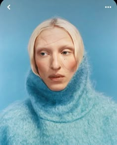 a woman with blonde hair wearing a blue turtle neck sweater and looking at the camera