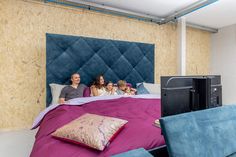 three people and two children sitting on a bed in a room with plywood walls