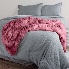 a bed with a pink blanket on top of it next to two pillows and blankets