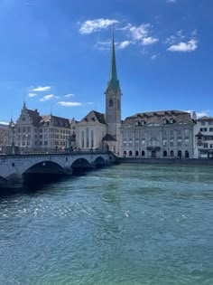 an old bridge crosses the water in front of some buildings and a church steeple