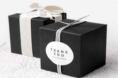 two black boxes with white ribbons and thank you tags