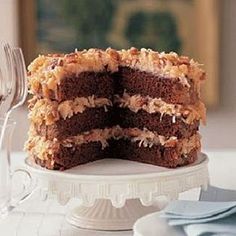 a chocolate cake is cut into pieces on a white plate with silverware and wine glasses