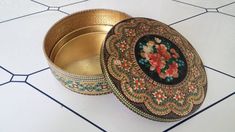 an ornately decorated metal box sitting on a tiled floor next to a vase with flowers in it