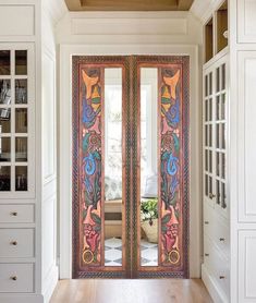 an ornately decorated double door in a white room with wood floors and built - in cabinets