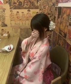 a woman in a kimono sitting at a desk with her hand on her face