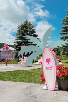 a pink and white surfboard sitting on top of a cement slab next to flowers