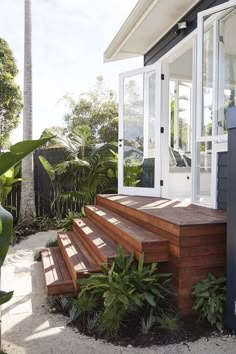 a house with wooden steps leading up to the front door and side porch, surrounded by greenery