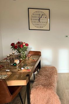 a room with a table, bench and clock on the wall above it that is decorated with flowers