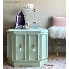 a white flower sitting on top of a green cabinet next to a pink pillow and chair