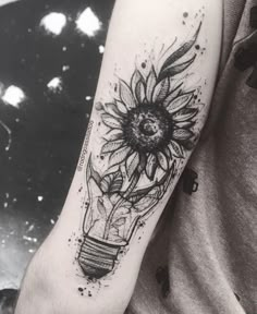 a black and white photo of a sunflower in a light bulb tattoo on the arm