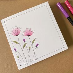 three pink flowers on a white card next to two markers and a marker pen,