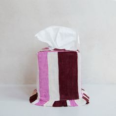 a pink and white striped toilet paper holder with tissue in it's center, on a white surface